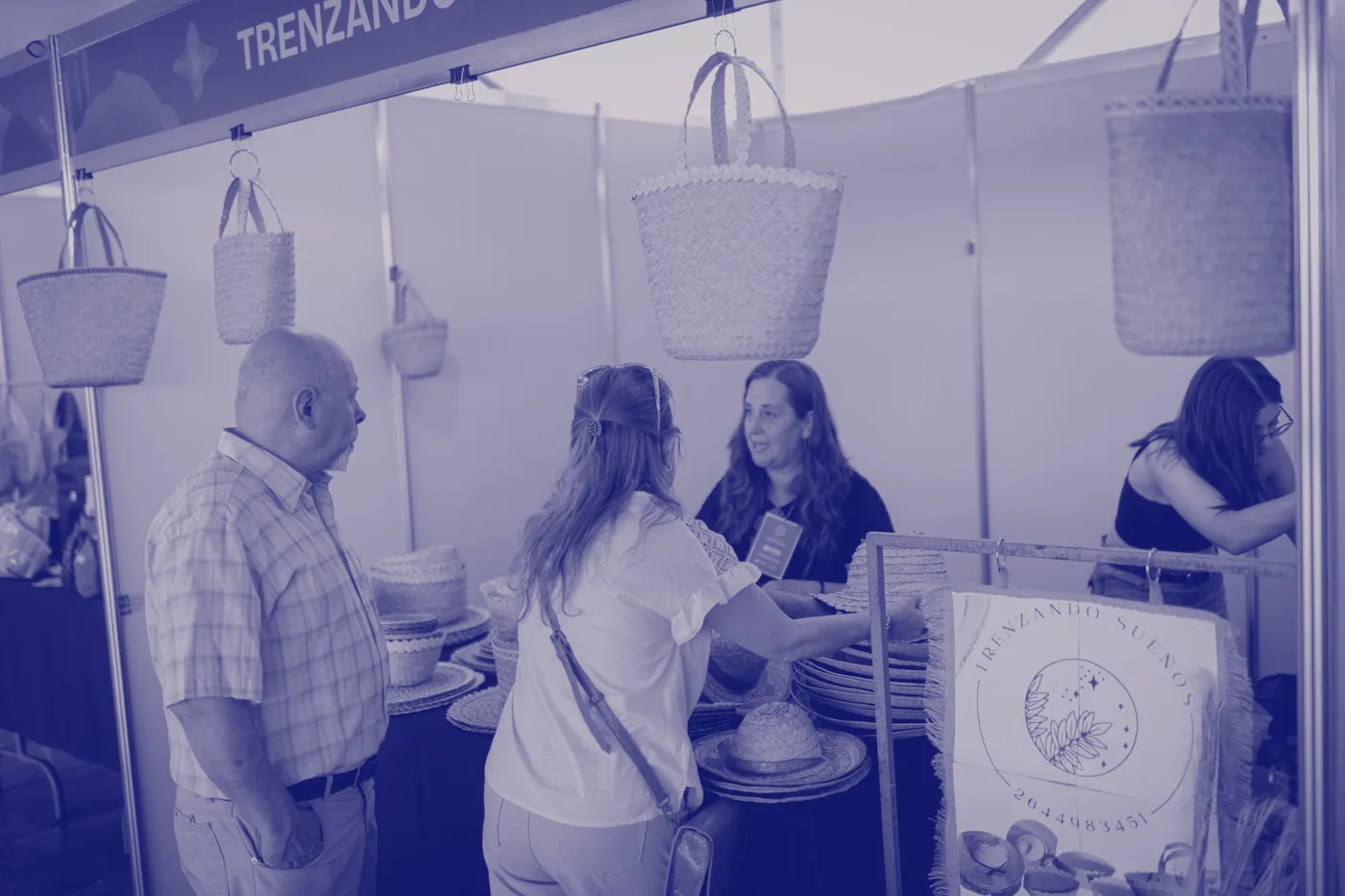 Una artesana mostrando sus cestos a dos visitantes en su stand
