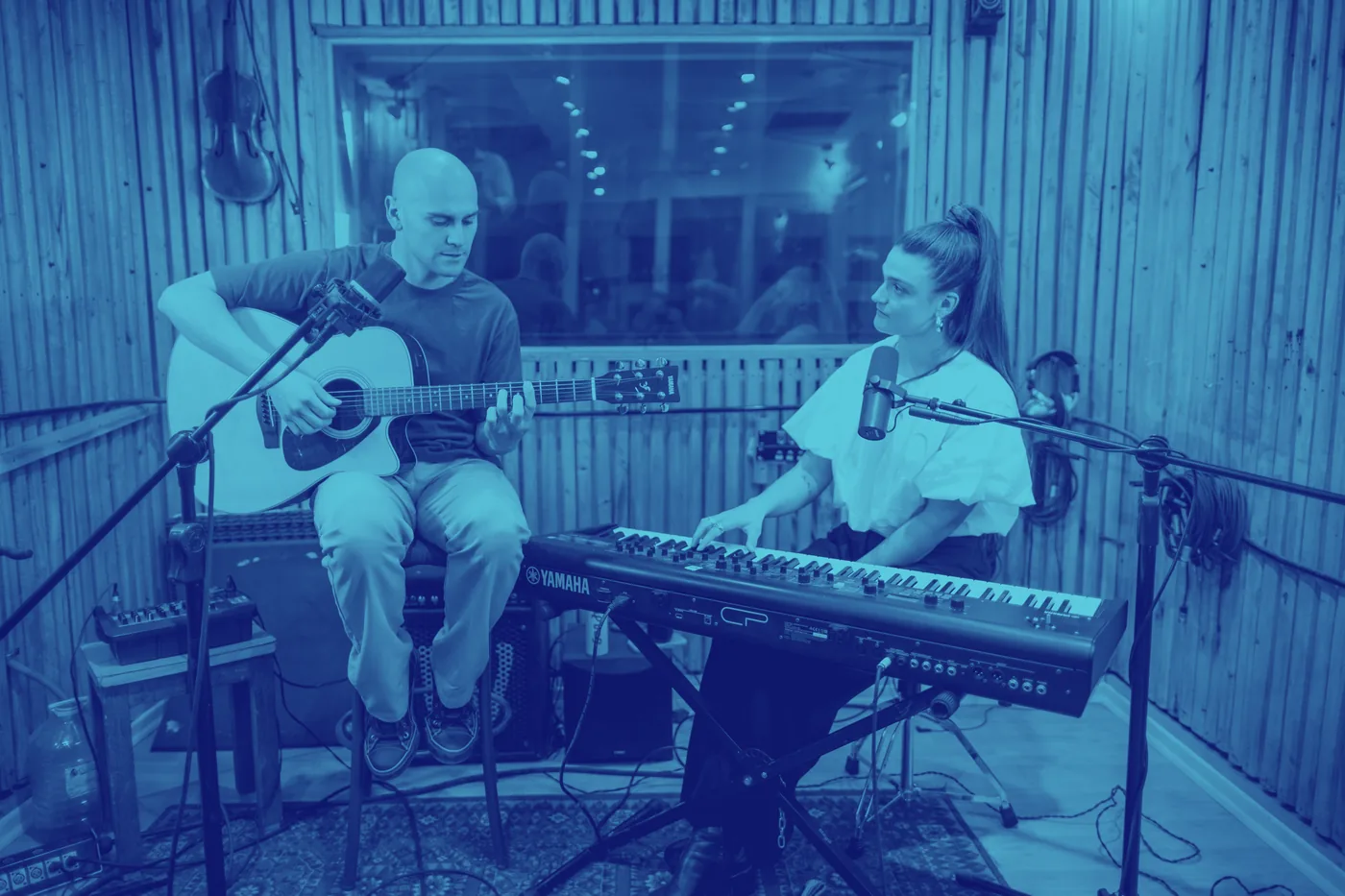 Un dúo tocando en un estudio de grabación: él con guitarra y ella al teclado